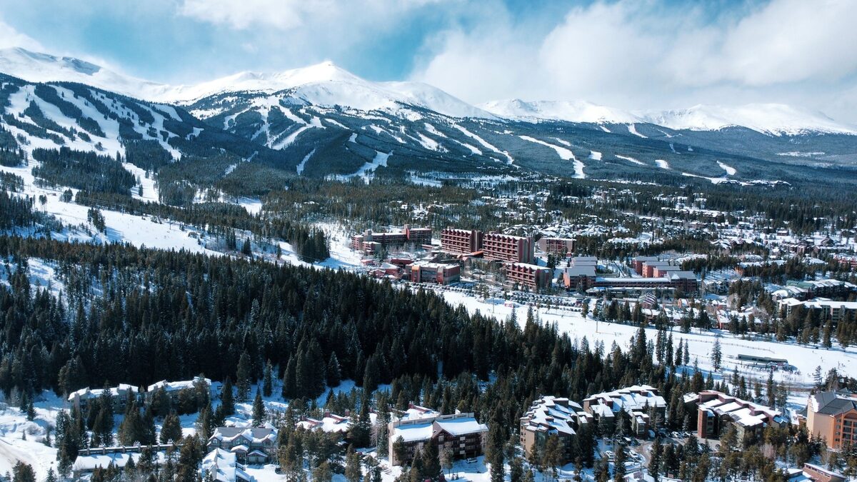 An aerial view of Breckenridge in winter, with the town's hotels and homes below the snowy ski runs of the Tenmile Range