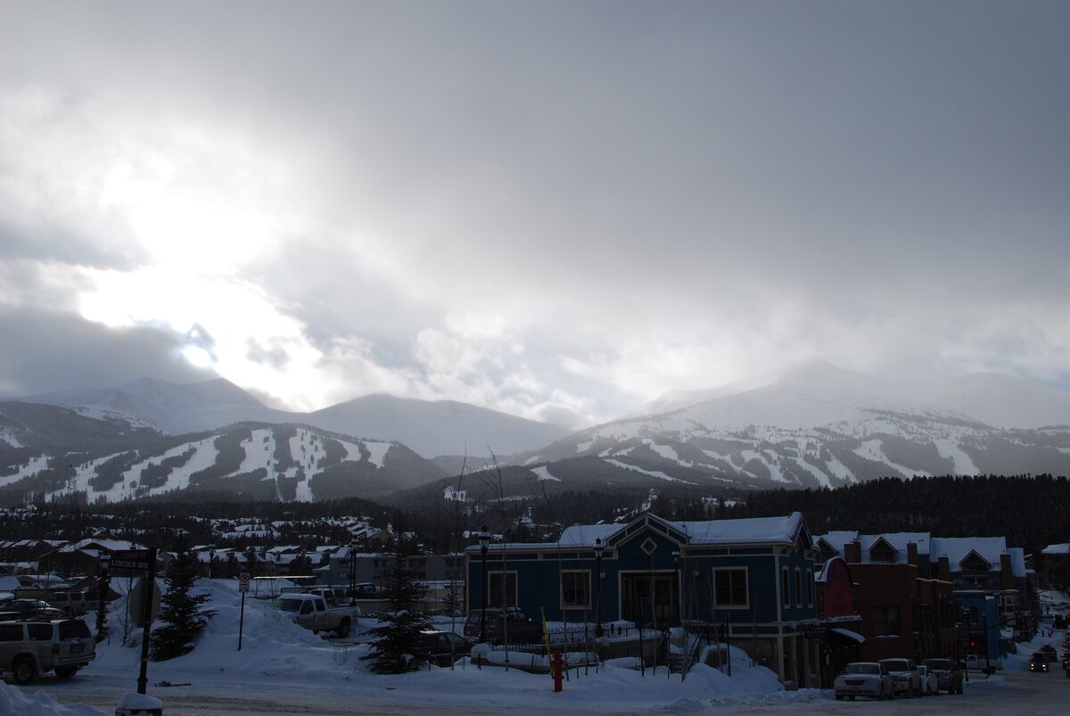 Breckenridge's town edge in winter, with the lit-up ski runs of the Tenmile Range rising behind the rooftops under heavy cloud