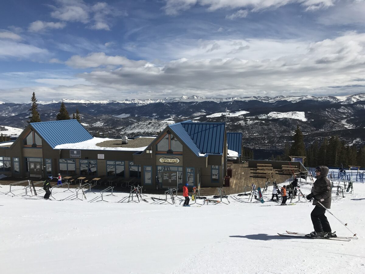Vista Haus at the Peak 8 base on a sunny day, with a skier on the groomed slope in front and the Tenmile Range behind