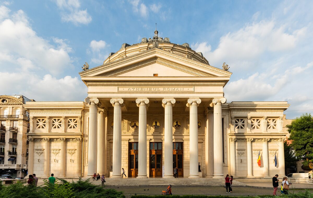 The Romanian Athenaeum by day, its six-columned portico and green dome against a blue sky with white clouds