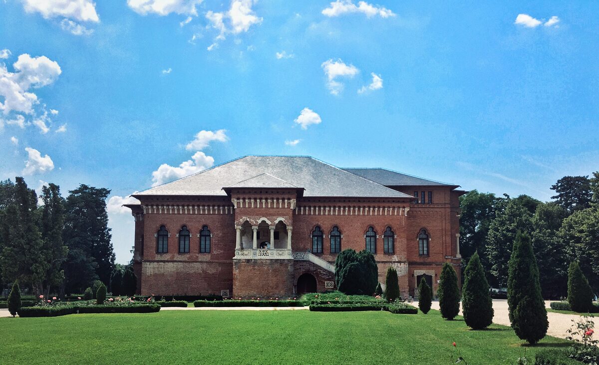 The red-brick Mogoșoaia Palace with its carved stone loggia and outside staircase, behind a clipped lawn and cypress trees