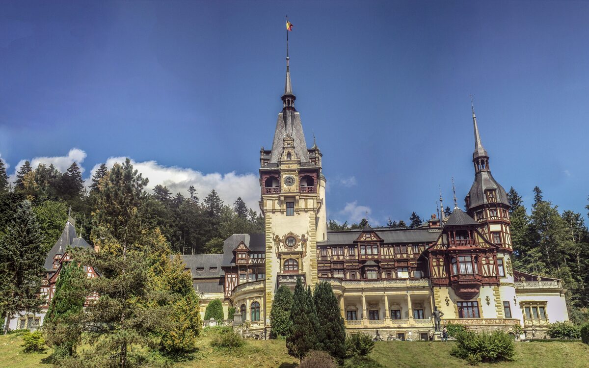Peleș Castle in Sinaia, a Neo-Renaissance palace with a tall central tower, timbered facades and spires, surrounded by fir trees