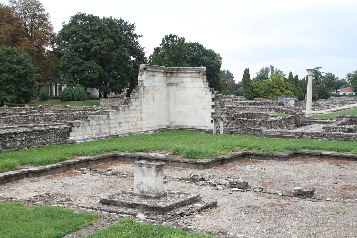 The excavated foundations of Roman Aquincum, with a partly rebuilt white stone wall and a single column on a lawn