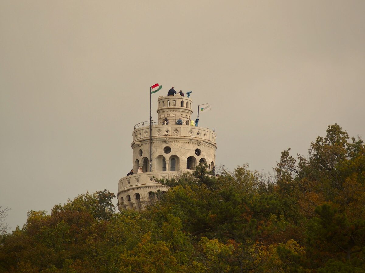 The round white Elizabeth Lookout with a Hungarian flag, rising above autumn treetops on János Hill