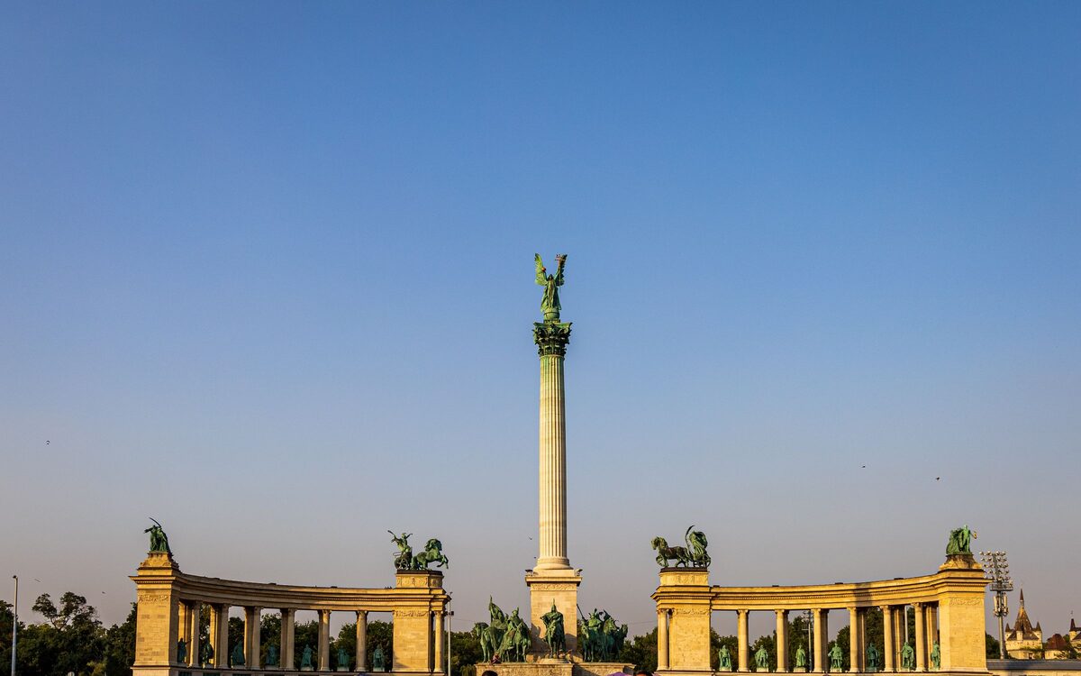 The Millennium Monument column topped by the Archangel Gabriel, between the two curved colonnades of Heroes' Square in warm evening light