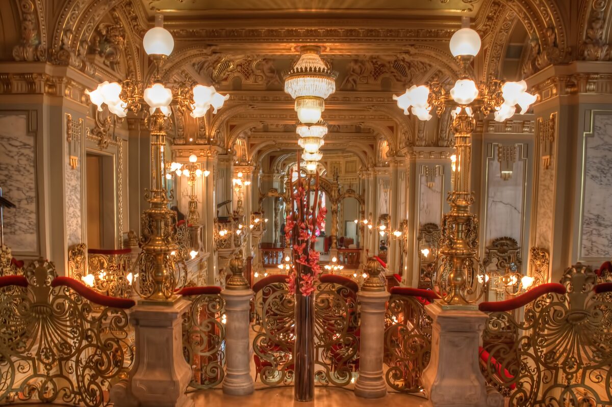 The gilded interior of the New York Café, with golden lamp posts, glowing globe lights and ornate railings