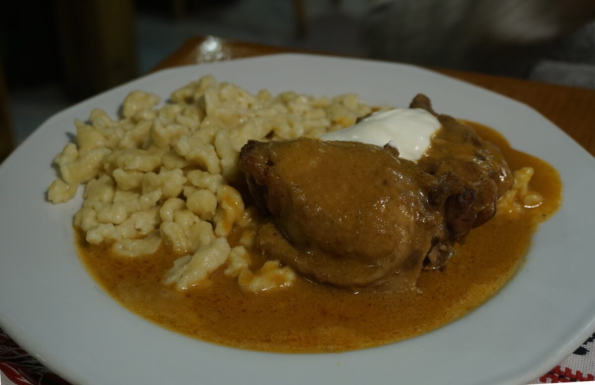 Chicken paprikash in a paprika sauce with a spoon of sour cream and nokedli dumplings on a white plate