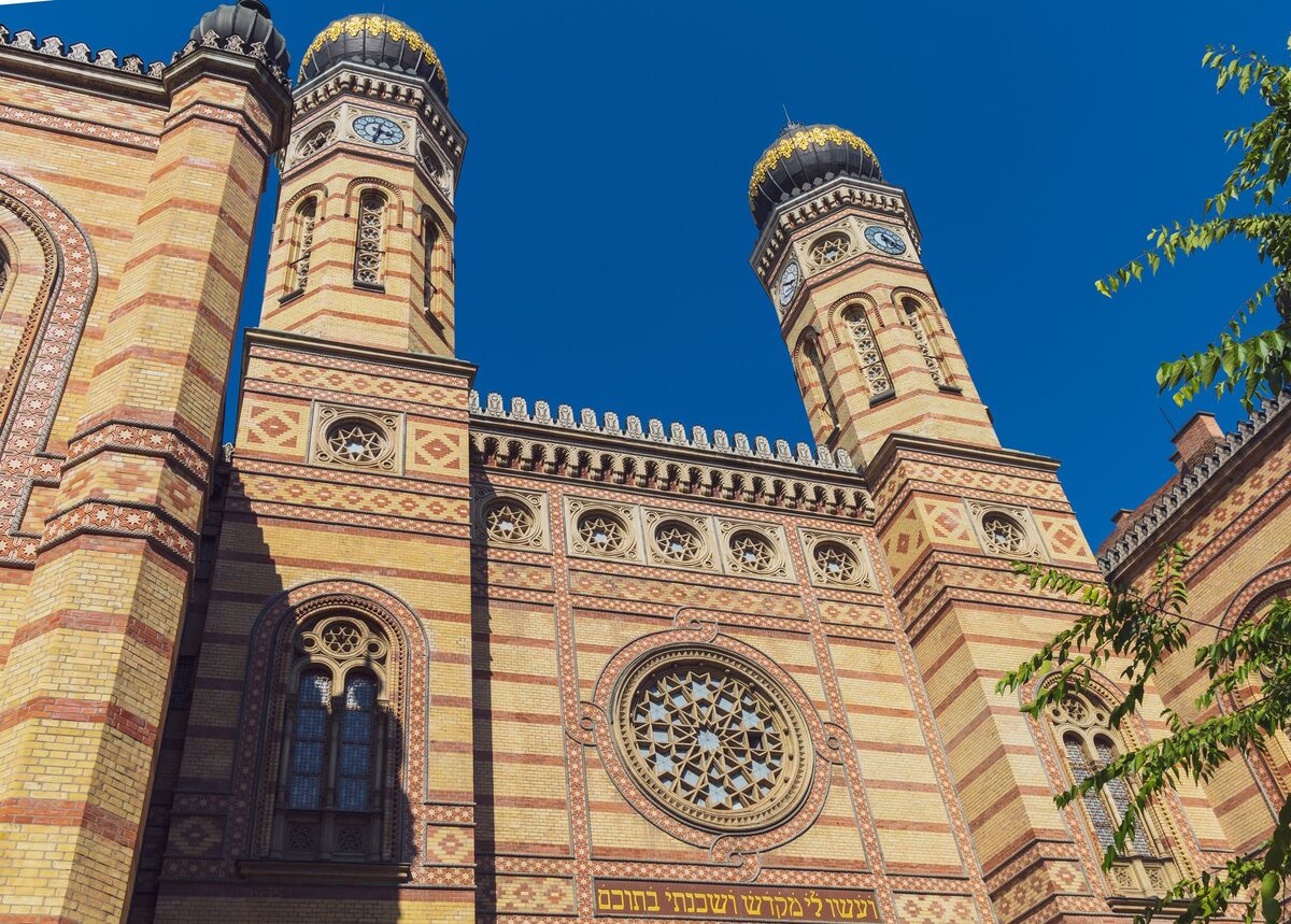 The striped brick facade, rose window and two onion-domed towers of the Dohány Street Synagogue under a deep blue sky