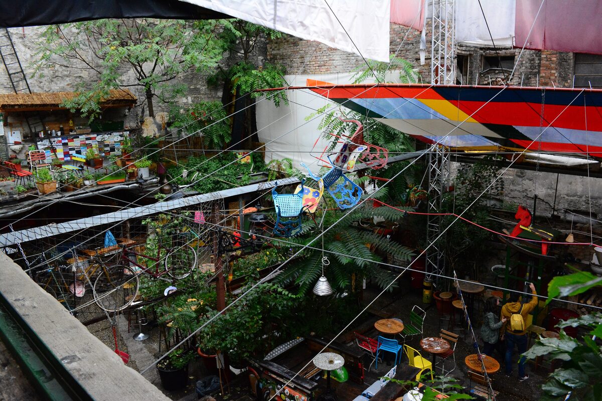 Looking down into the Szimpla Kert courtyard, a tangle of plants, wires, old bicycles, a hanging boat and mismatched chairs
