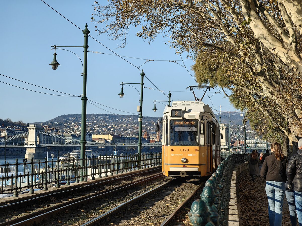 A yellow tram on line 2 along the Pest embankment, with the Chain Bridge and the Buda hills across the Danube