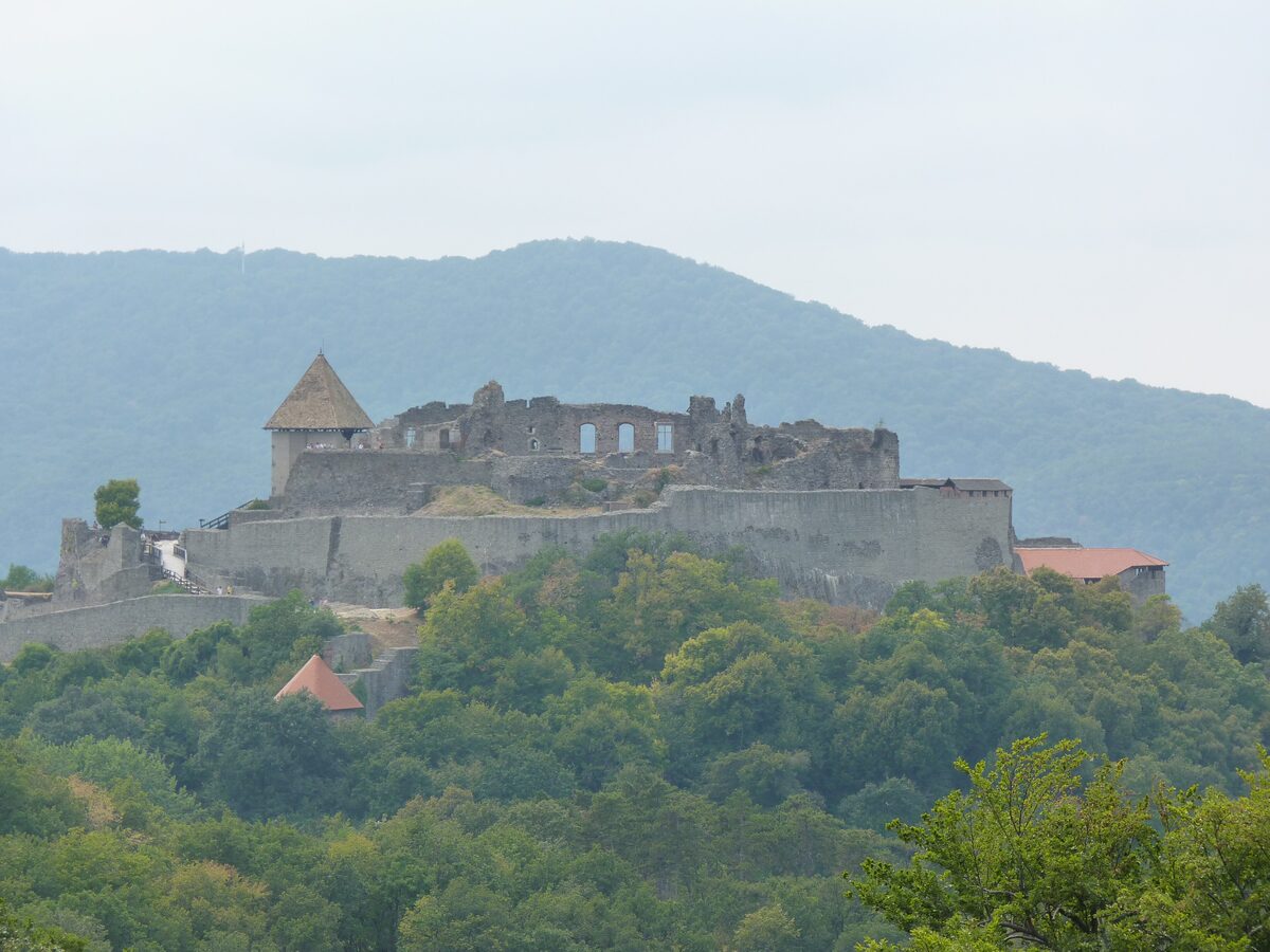 The stone walls and tower of Visegrád's upper citadel on a wooded hilltop, with forested hills behind