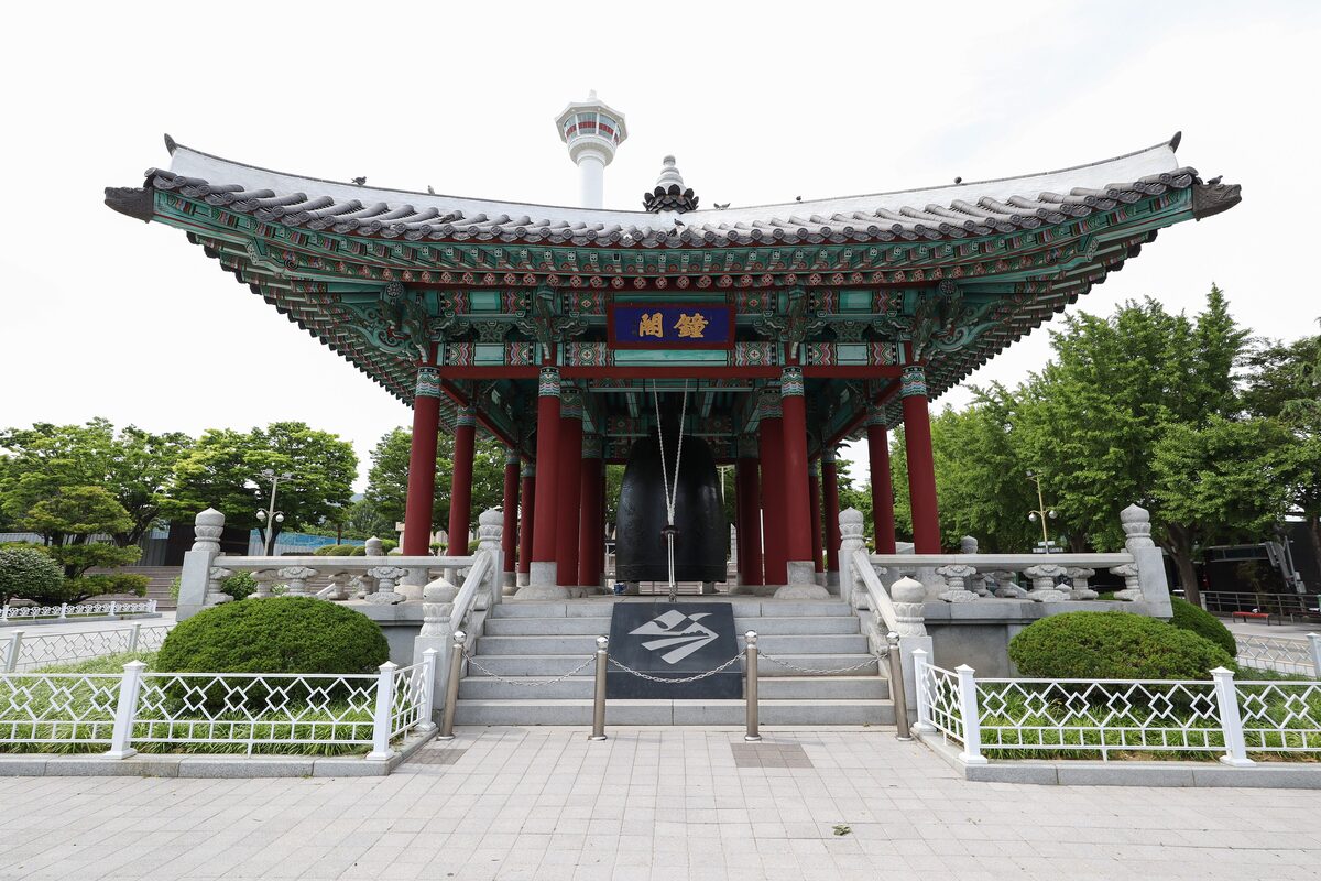 Busan Tower rising above the roof of a red-pillared pavilion in Yongdusan Park