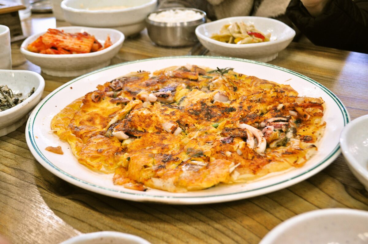 A golden seafood and green onion pancake on a white plate at a restaurant table
