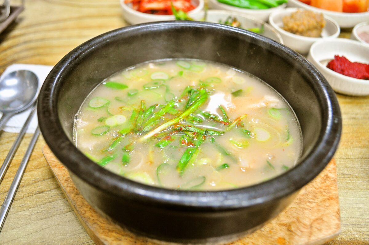 A stone bowl of pale pork and rice soup topped with green onion, served with side dishes