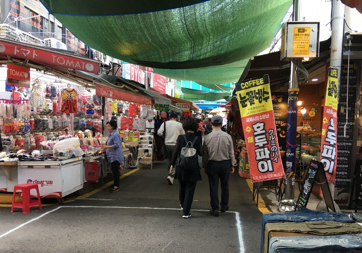 A covered alley in Gukje Market under a green canopy, with stalls and shoppers on both sides