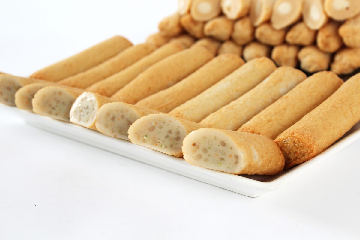 Rows of golden fish-cake rolls laid out on a white tray, some cut open to show the filling