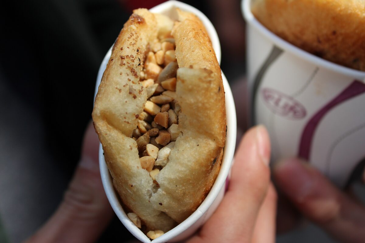 A ssiat hotteok pancake held in a paper cup, split open to show the seeds and nuts inside