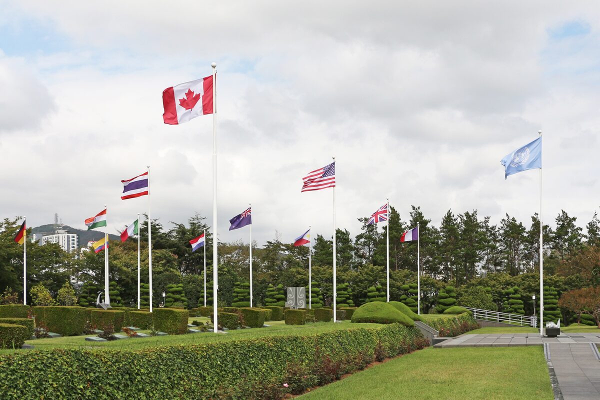 Rows of national flags on tall poles over clipped lawns at the UN Memorial Cemetery in Busan