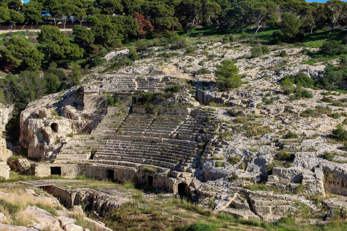 Rows of seats carved into the limestone hillside of the Roman Amphitheatre, with pines above