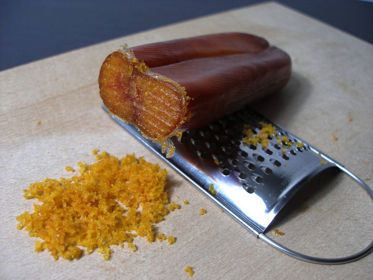 A cut piece of mullet bottarga beside a pile of the golden grated powder on a metal grater