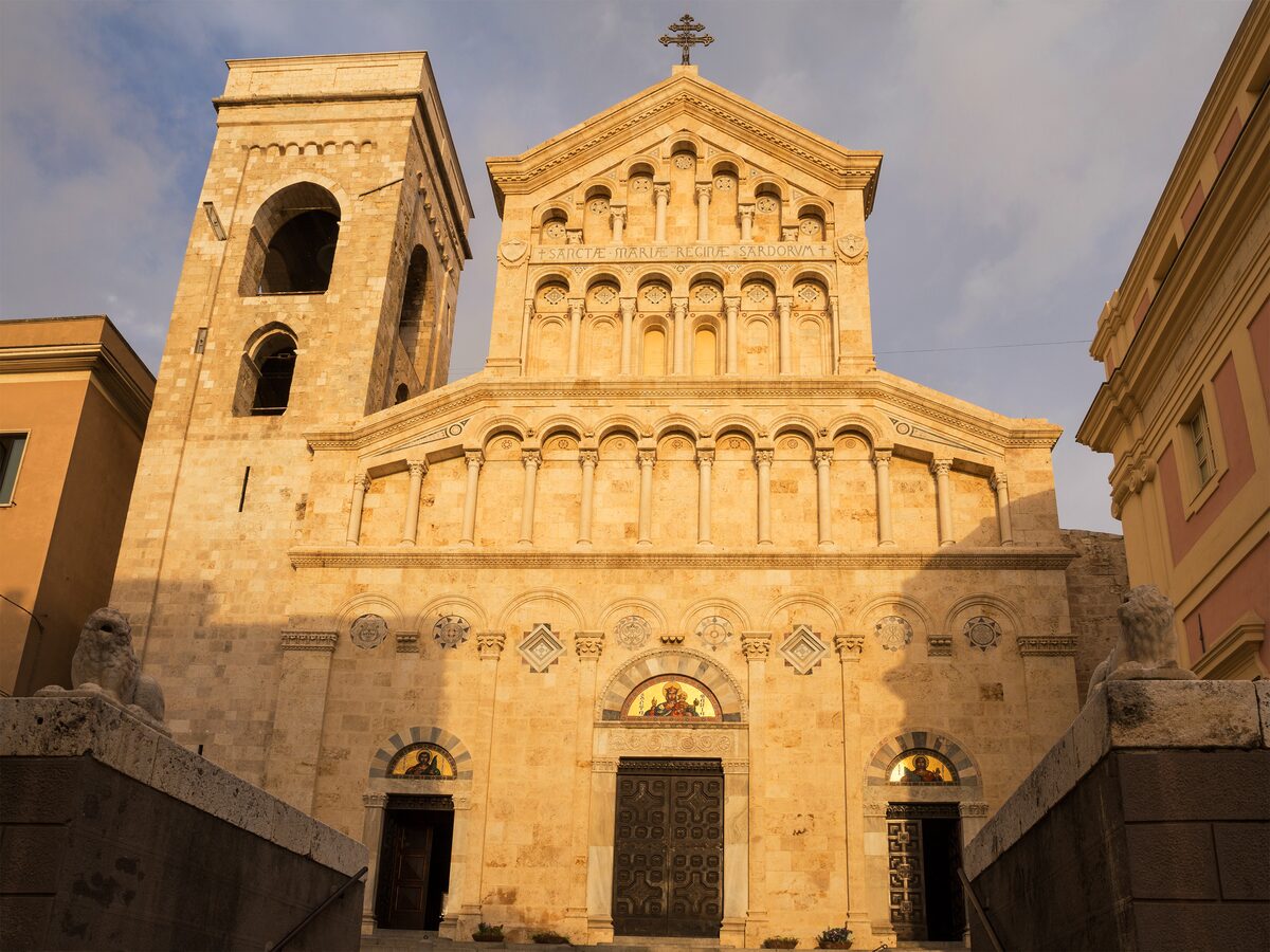The golden Pisan-style Romanesque facade of Cagliari Cathedral with its bell tower, lit by late sun