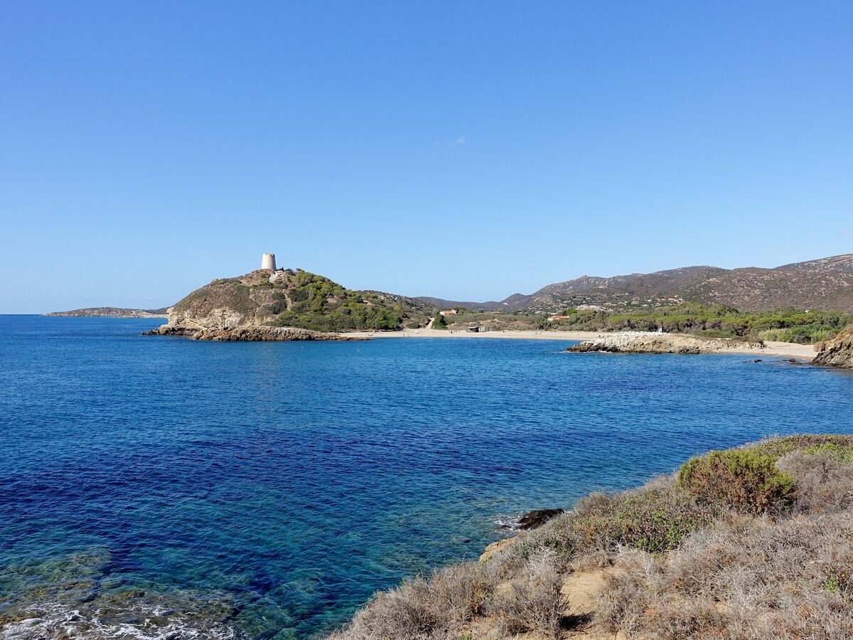 The headland with the Tower of Chia above turquoise water and a curve of pale sand on Chia's coast