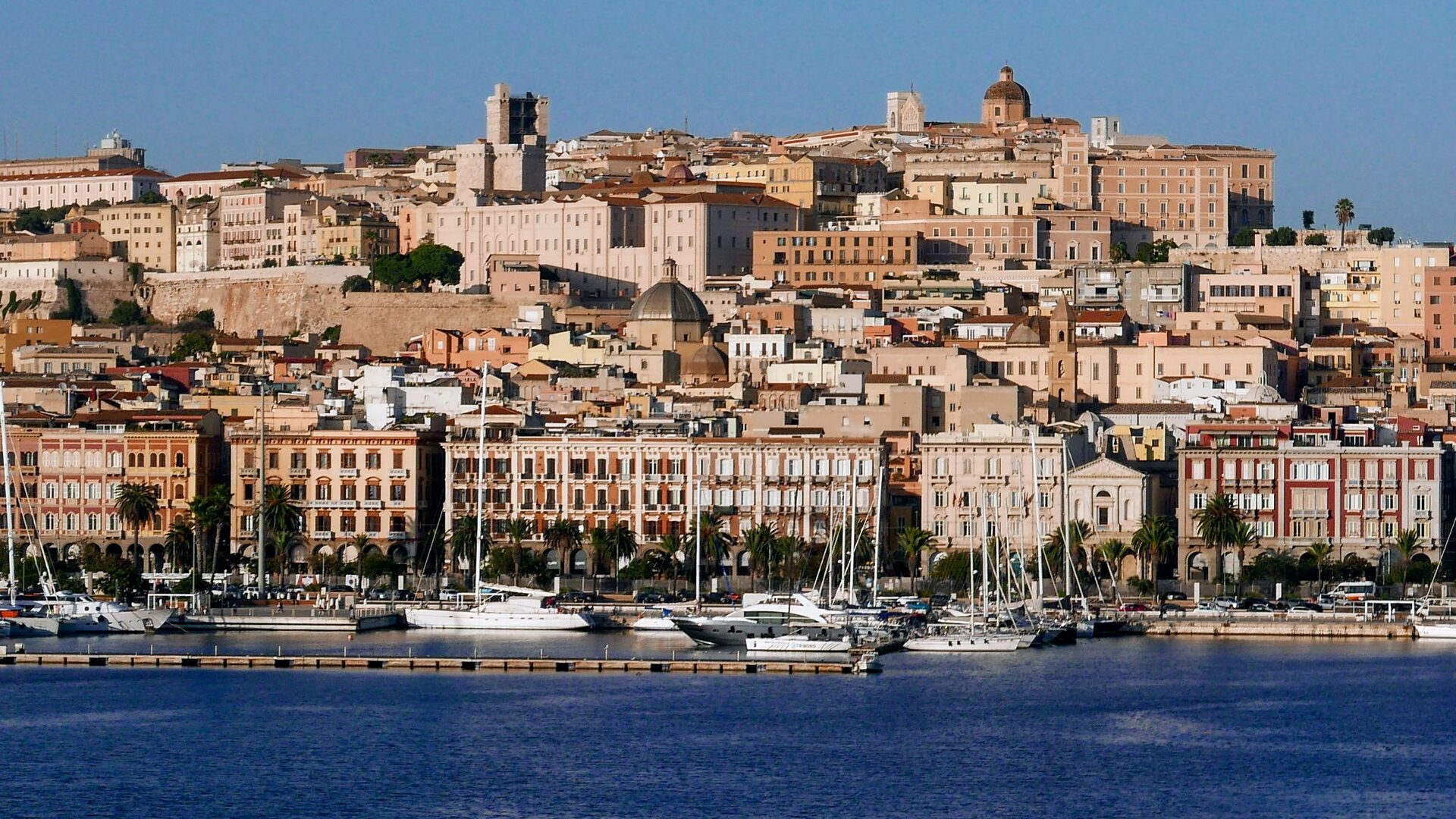 The Castello hill of Cagliari above the marina, with pastel waterfront buildings and the cathedral dome