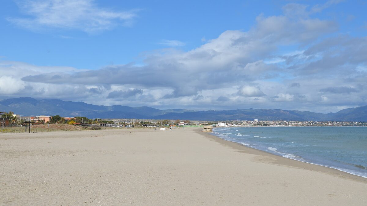 The long, wide sand beach of Poetto stretching along the bay under a blue sky with clouds