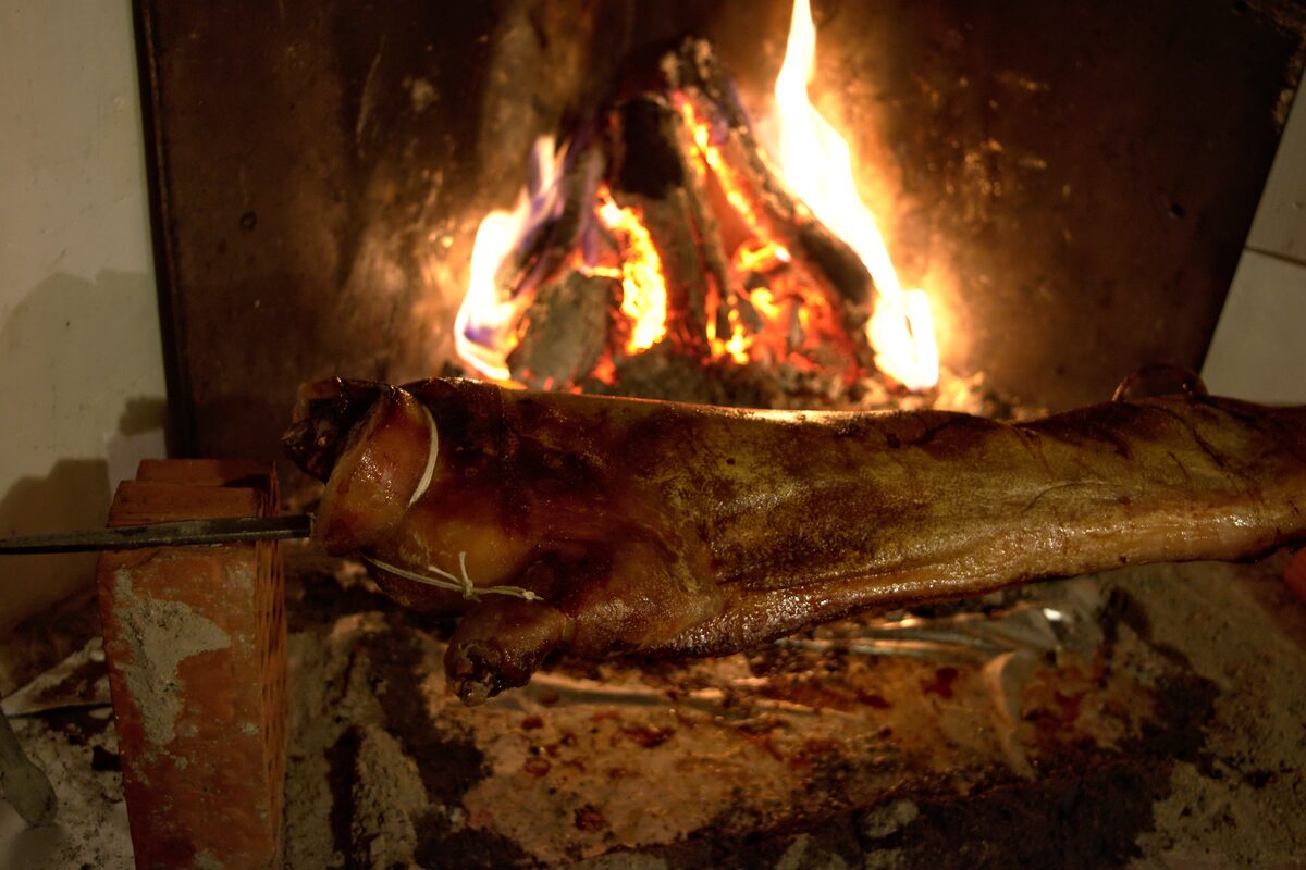 A whole suckling pig roasting on a spit in front of an open wood fire