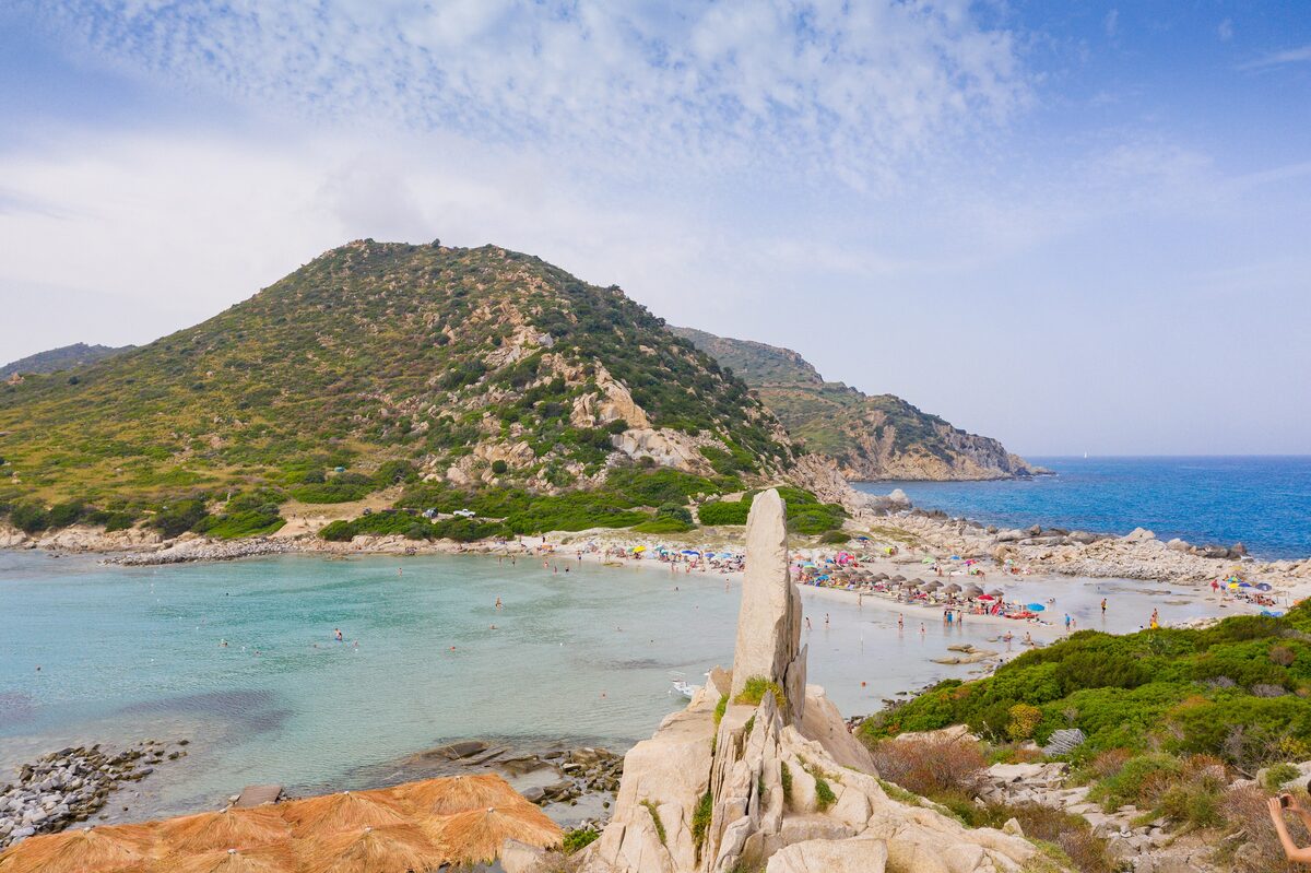 The sheltered turquoise bay of Punta Molentis seen past a granite spire, with the green headland behind