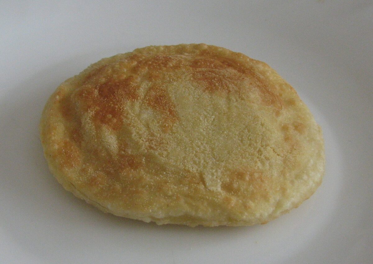 A single golden fried seada, the round Sardinian pastry, on a white plate