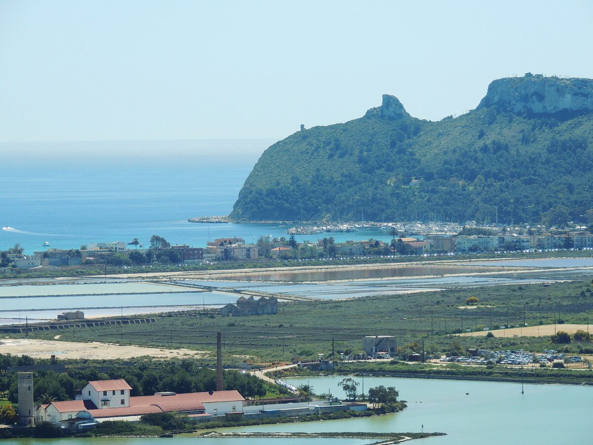 The Sella del Diavolo headland rising from the sea above a small harbor, with salt pans and wetlands in front