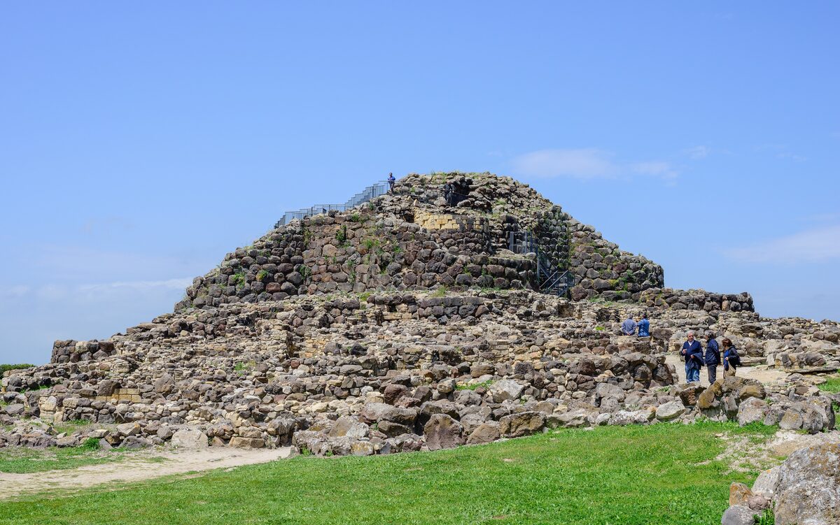 The stone mound of the Su Nuraxi nuraghe rising above a grassy path under a blue sky