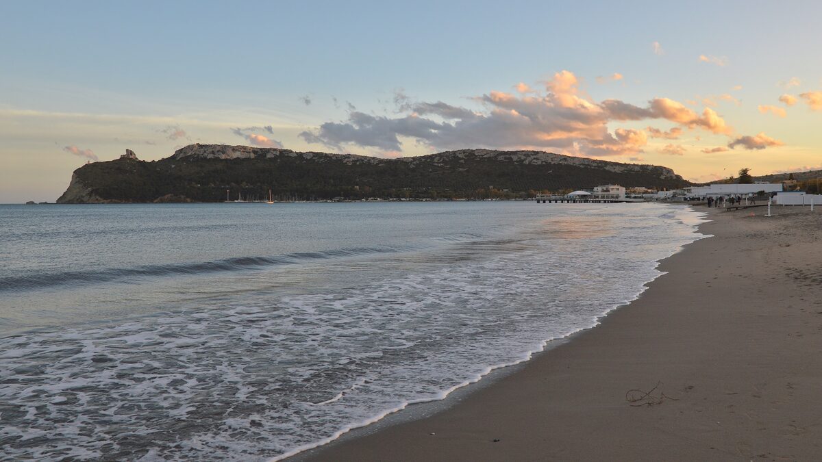 Evening light on Poetto beach, with waves on the sand and the Sella del Diavolo headland across the bay