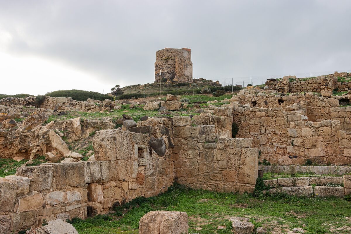 The excavated stone walls of Tharros with a stone watchtower on the hill above
