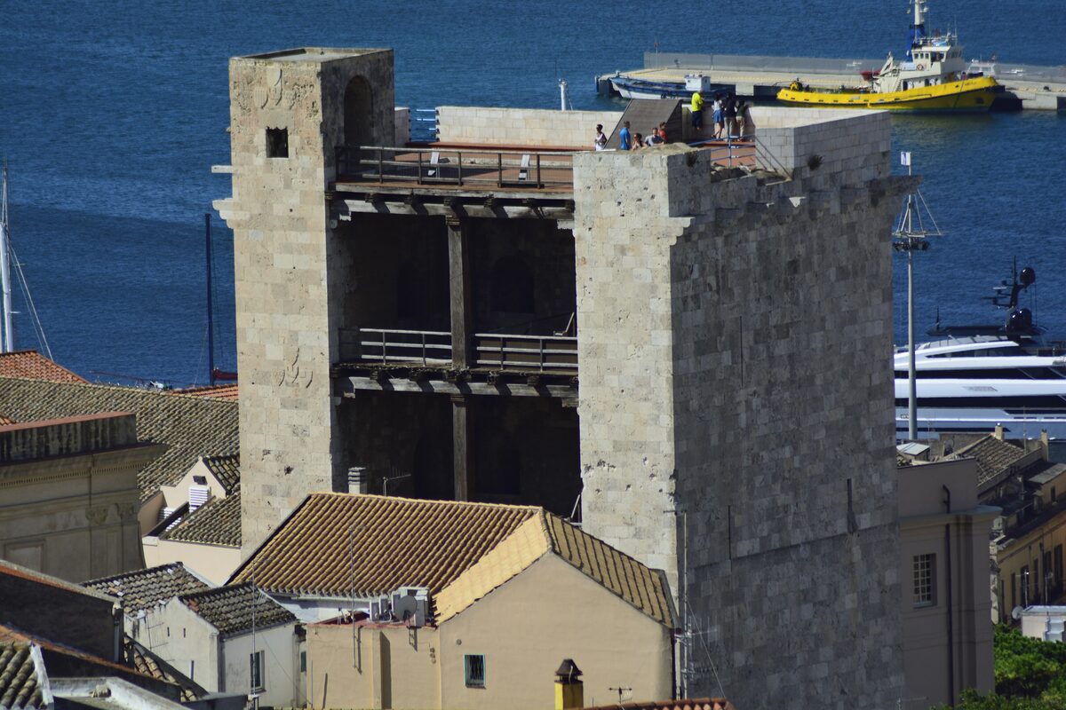 The Torre dell'Elefante, a square medieval stone tower with an open wooden top, above rooftops and the harbor