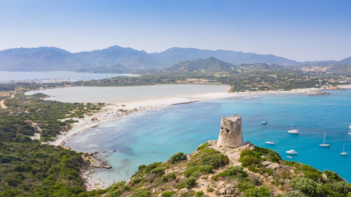 The Torre di Porto Giunco on its rocky hilltop above the curving bay, the Notteri pond and the Sarrabus mountains beyond