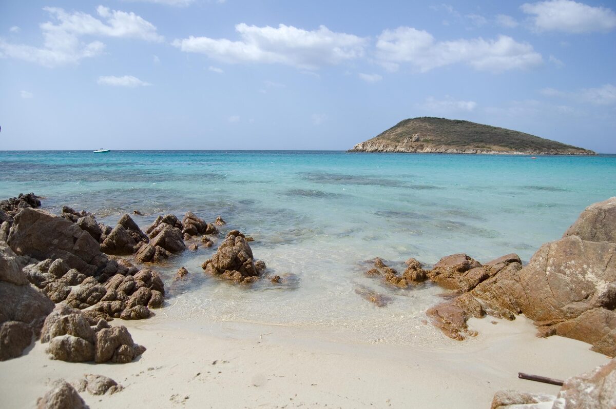 Clear turquoise water and white sand at Tuerredda, with granite rocks in front and the small island offshore
