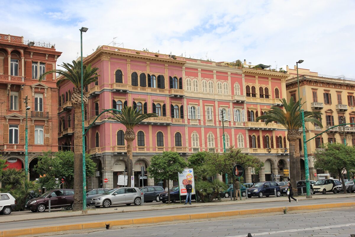 The arcaded pink and ochre palazzi of Via Roma along the waterfront, with palm trees in front