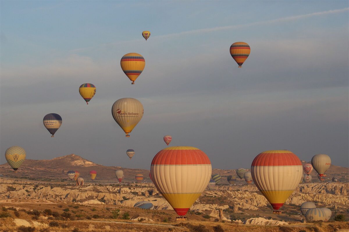 Colorful hot-air balloons, two big striped ones close to the ground, drifting over Göreme's pale valleys at sunrise