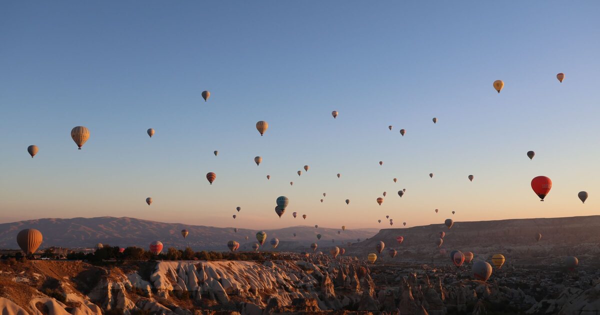 Dozens of hot-air balloons in a clear dawn sky over the fairy chimneys of Göreme, lit orange by the rising sun