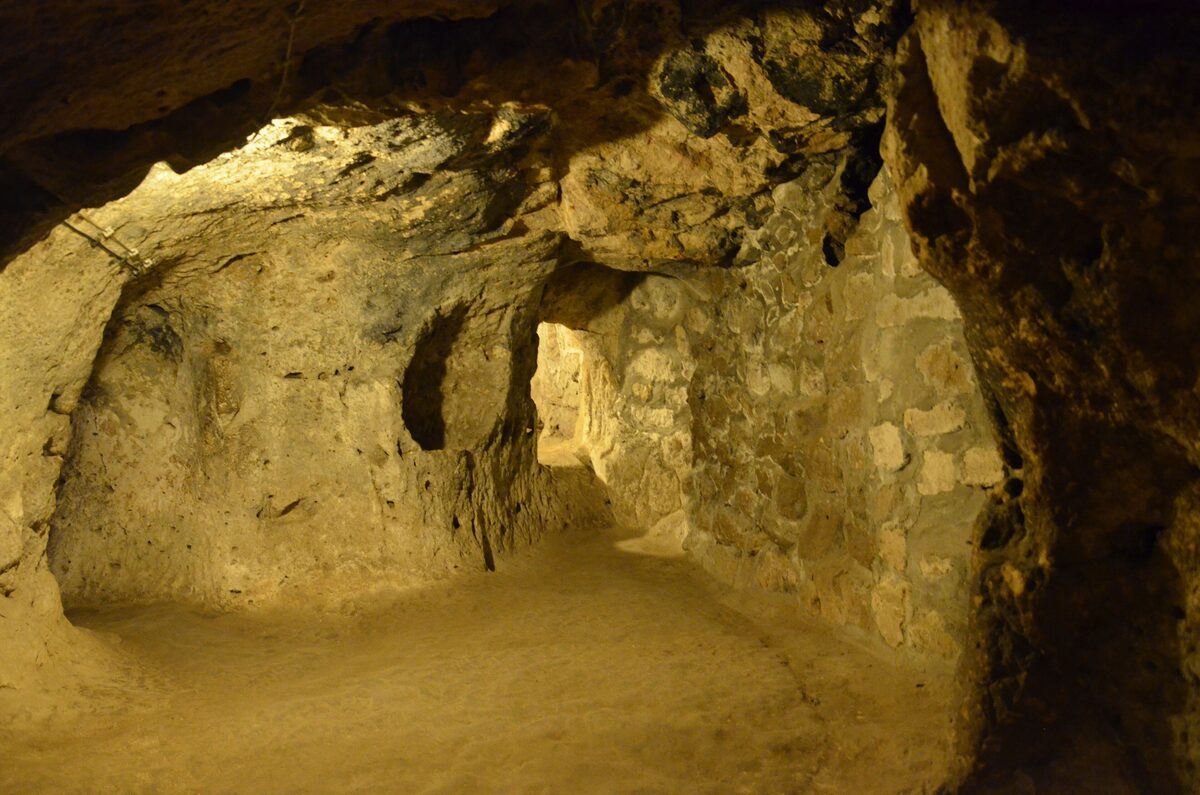 A lamp-lit tunnel and chamber cut into soft yellow rock inside the Derinkuyu underground city