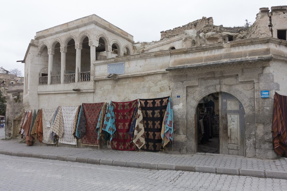 A stone Greek mansion in Mustafapaşa with an arched upper loggia and carpets hung along the street