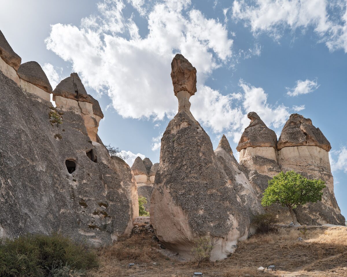 The mushroom-capped fairy chimneys of Paşabağ, one balancing a slim stone cap, under a cloudy blue sky