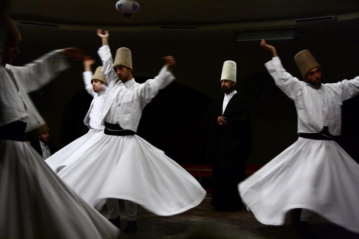 Whirling dervishes in white robes and tall felt hats turning in a dark hall in Avanos