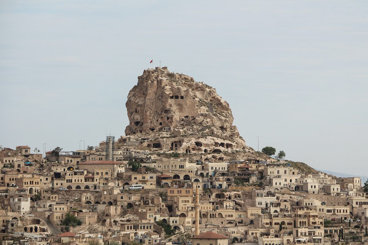 The rock of Uçhisar Castle, riddled with caves and topped by a Turkish flag, above the stone houses of the village