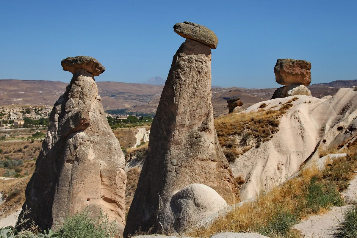 The Three Beauties of Ürgüp, tall fairy chimneys with dark stone caps against a blue sky