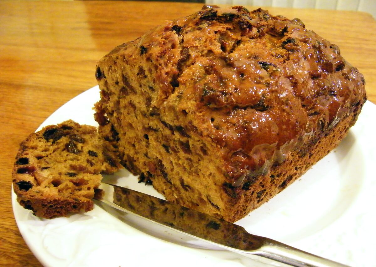 A loaf of bara brith, a dark fruit tea loaf, with a slice cut on a plate