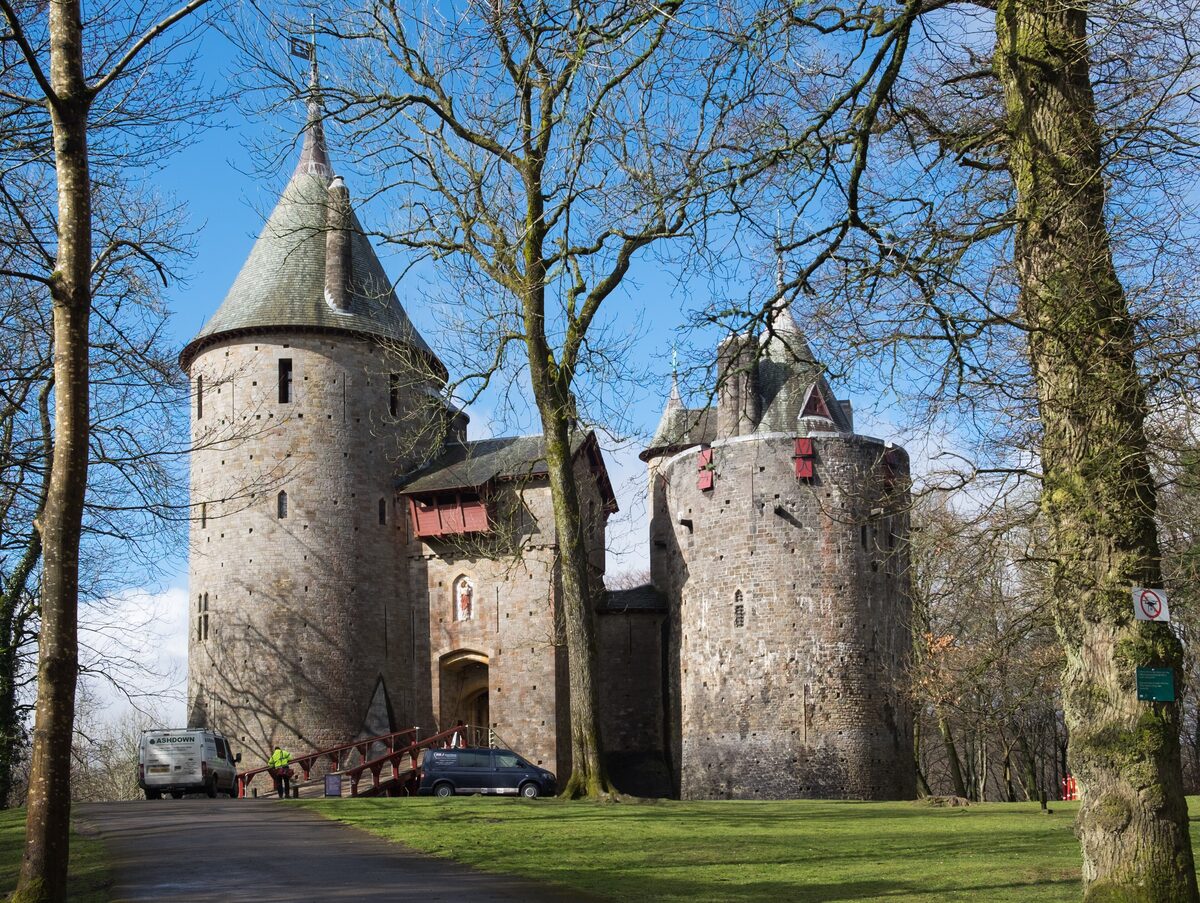 Castell Coch, a red sandstone castle with conical turret roofs, rising from a beech wood on a hillside