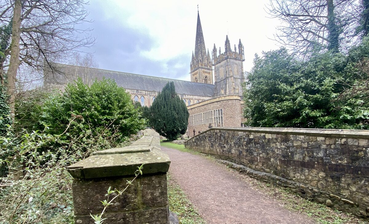 Llandaff Cathedral with its tower and spire, seen along a path between trees and an old wall